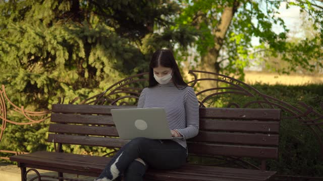 Woman-in-medical-protective-mask-freelancer-working-with-laptop-outdoor-in-park