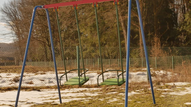 swing-on-a-playground-near-the-forest.-wind-is-moving-it.-no-kids.