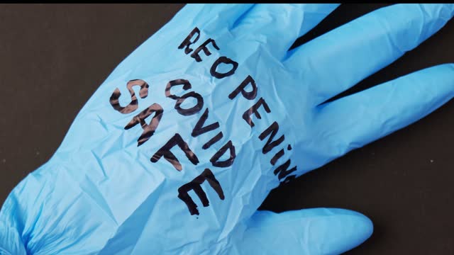 Blown-up-blue-latex-surgical-glove-on-black-background.-Reopening-covid-safe.-Open-again-text-written-on-medical-glove.-New-normal