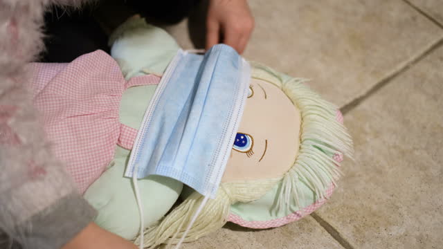 Kleines-Kind-Tochter-spielen-mit-Puppe-Rollenspiel-Gesichtsmaske-tragen-zu-Hause,covid19
