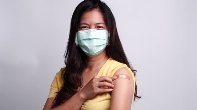 Frau-trägt-medizinische-Gesichtsmaske-zeigt-ihren-Arm,-nachdem-sie-mit-dem-Gefühl-glücklich-geimpft.-Konzept-der-Impfung,-geimpfte-Patienten,-Impf-Roll-out-Programm,-Coronavirus,-COVID-19.