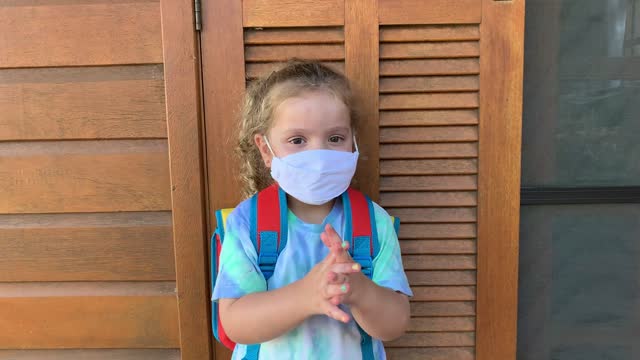 Kleines-Mädchen-immer-bereit-fot-Schule-mit-Handdesinfektionsmittel-und-schützende-Gesichtsmaske-während-Covid-19.
