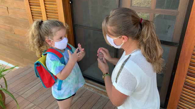 Kleines-Mädchen-und-Mutter-immer-bereit-fot-Schule-mit-Handdesinfektionsmittel-und-schützende-Gesichtsmaske-während-Covid-19.