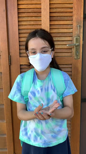 Little-girl-getting-ready-fot-school-using-hand-sanitizer-and-protective-face-mask-during-Covid-19.-Vertical-format-video