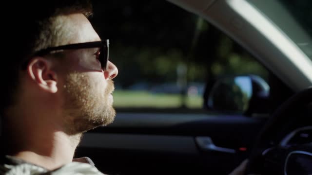 A-man-is-driving-a-modern-car.-A-handsome-man-with-a-beard-in-the-sun-protective-glasses,-confidently-steers