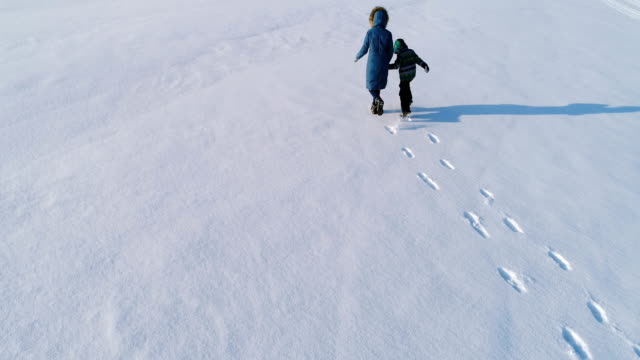 Family-time-walk-and-play-together.-Mother-and-son-running-hand-in-hand-through-the-snow-covered-area-in-winter.-back-view.