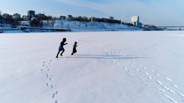 Mama-und-Sonne-ist-laufen-und-spielen-zusammen-im-Schnee.-Luftaufnahmen.-Familie-Zeitvertreib-im-Winter.