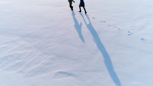 Mama-und-Sonne-laufen-zusammen-im-Schnee.-Luftaufnahmen.-Familie-Zeitvertreib-im-Winter.
