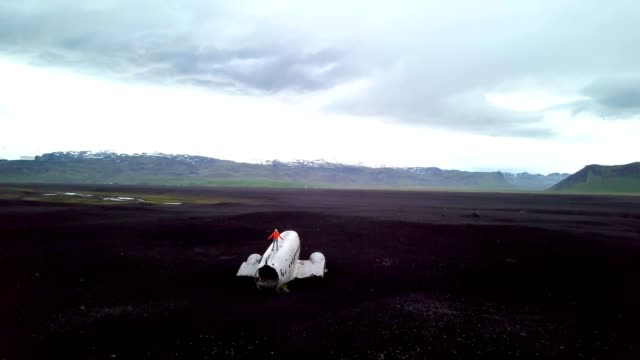 Mujer-joven-está-parado-brazos-extendidos-en-avión-que-se-estrelló-en-la-playa-de-arena-negra-mirando-su-contemplación-lugar-famoso-entorno-para-visitar-en-Islandia-y-posan-junto-a-los-restos-del-naufragio-4K-video