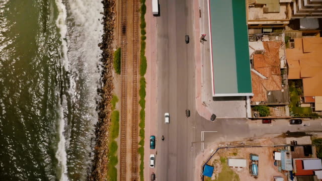 Drone-flying-along-coast-line-street-in-Colombo,-Sri-Lanka.-Aerial-shot-of-cars,-buildings,-ocean-waves-and-railroad