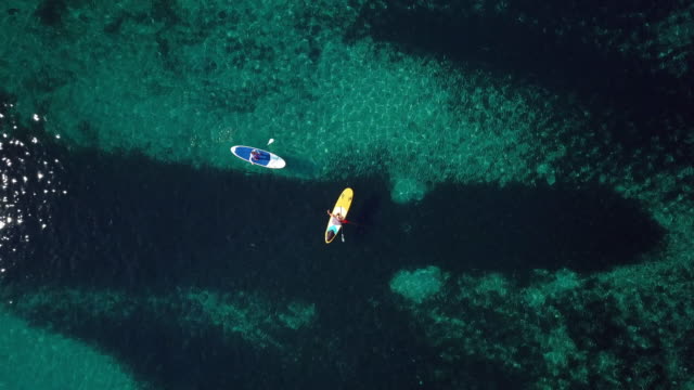 Video-from-above,-aerial-view-of--two-people-on-a-stand-up-paddle-(SUP)-in-Sardinia,-Italy.