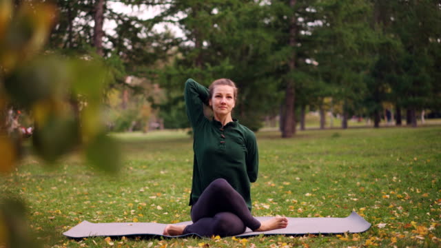 Cheerful-lady-is-exercising-in-park-sitting-in-Cow-Face-pose-with-arms-behind-her-back-during-outdoor-practice-in-city-park.-Nature,-millennials-and-health-concept.