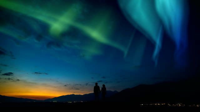 The-man-and-a-woman-standing-on-a-mountain-against-a-northern-light.-time-lapse