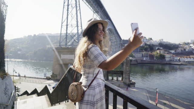 Lady-in-hat-taking-selfie-on-smartphone-on-embankment