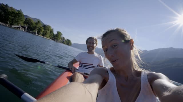 Junges-Paar-in-den-Sommerferien-Kanu-auf-dem-See-in-den-Bergen-zu-genießen.-Die-Leute-Reisen-Spaß-Urlaub-Konzept.-Technologie-und-Jugendkultur-nehmen-Selfie---4K
