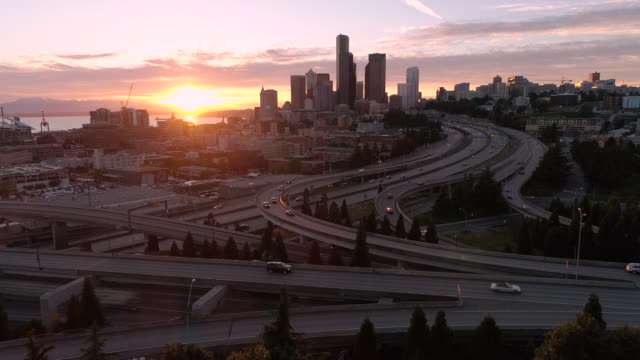 Drohne-Schuss-von-Seattle-mit-epischen-glühenden-Sonnenuntergang-auf-Autobahn-und-Innenstadt-Wolkenkratzer-Gebäude-in-der-Skyline-der-Stadt