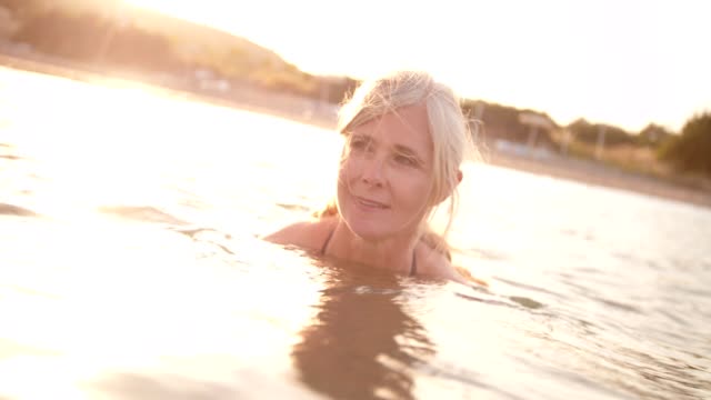 Mujer-senior-activa-nadando-en-el-mar-al-atardecer