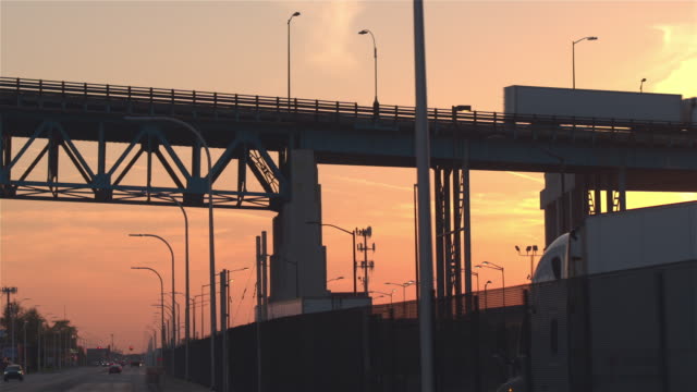 CLOSE-UP:-Silhouetted-cars-and-trucks-driving-through-industrial-town-at-sunset