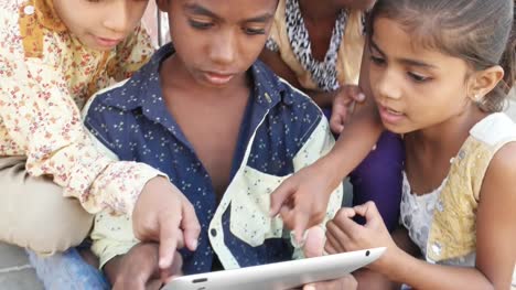 Indian-Kids-busy-on-a-touchscreen-tablet,-elder-sibling-teaching-them,-close-up-handheld