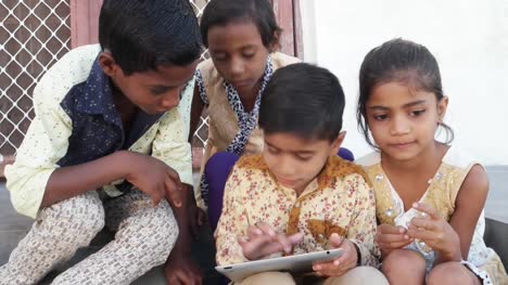 Indian-Kids-busy-on-a-touchscreen-tablet,-elder-sibling-teaching-them,-close-up-handheld