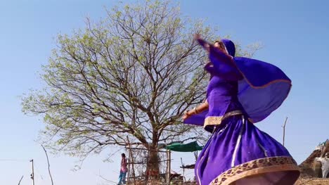 Mujer-remolino-redondo-azul-ropa-india-tradicional-en-un-desierto-frente-a-un-árbol.