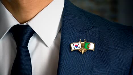 Geschäftsmann-zu-Fuß-in-Richtung-Kamera-mit-Freund-Land-Flaggen-Pin-Südkorea---Algerien