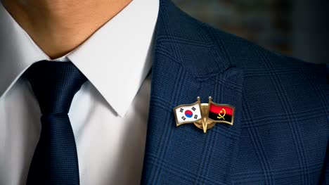Geschäftsmann-zu-Fuß-in-Richtung-Kamera-mit-Freund-Land-Flaggen-Pin-Südkorea---Angola