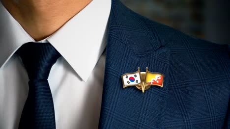 Empresario-caminando-hacia-cámara-con-amigo-país-banderas-Pin-Corea-del-sur---Bhután