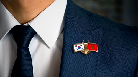 Geschäftsmann-zu-Fuß-in-Richtung-Kamera-mit-Freund-Land-Flaggen-Pin-Südkorea---Marokko