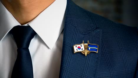 Businessman-Walking-Towards-Camera-With-Friend-Country-Flags-Pin-South-Korea---Nauru