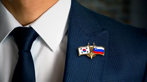 Businessman-Walking-Towards-Camera-With-Friend-Country-Flags-Pin-South-Korea---Slovenia