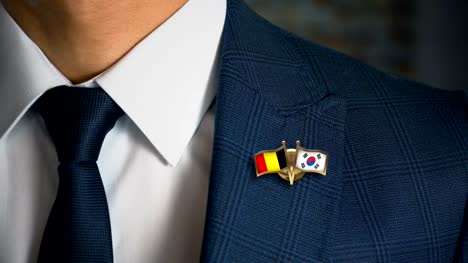 Empresario-caminando-hacia-cámara-con-amigo-país-banderas-Pin-Bélgica---Corea-del-sur