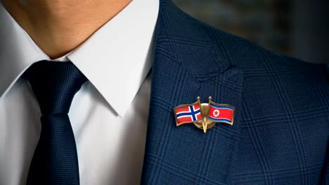 Empresario-caminando-hacia-cámara-con-amigo-país-banderas-Pin-Noruega---Corea-del-norte