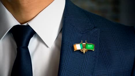 Geschäftsmann-zu-Fuß-in-Richtung-Kamera-mit-Freund-Land-Flaggen-Pin-Irland---Saudi-Arabien