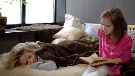 Daughter-reads-the-book-on-the-bed-while-mom-sleeps.