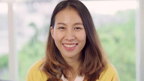 Teenager-asiatische-Frau-glücklich-lächelnd-und-Blick-auf-Kamera,-während-in-ihrem-Wohnzimmer-zu-Hause-entspannen.-Schöne-asiatische-junge-Frauen-mit-entspannen-Zeit-im-Wohnkonzept.