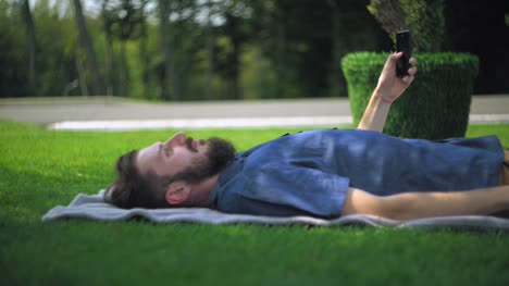 Hombre-de-reclinación-con-smartphone-al-aire-libre