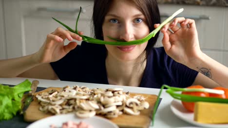schöne-lustige-Frau-Koch-spielen-mit-grüner-Zwiebel-auf-dem-Tisch-in-der-Küche-zu-Hause