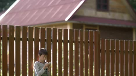 Junge-steht-verwendet-eine-Telefon-in-der-Nähe-einen-Zaun-im-Dorf
