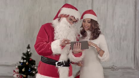 Weihnachtsmann-und-schöne-junge-lächelnde-Frau-mit-tablet