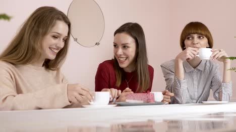 Three-young-Caucasian-girls-sitting-in-a-cafe,-drinking-coffee,-eating-cake,-smiling,-laughing,-gesturing-with-their-hands,-gossip-old-girlfriends-in-a-cafe-concept.-60-fps