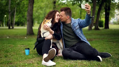 Handsome-young-man-is-taking-selfie-with-his-girlfriend-who-is-holding-pedigree-dog,-guy-is-kissing-girl-then-watching-photos-on-screen,-people-are-laughing.