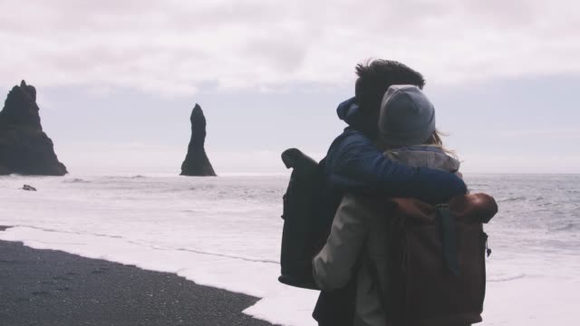 Pareja-joven-abrazos-y-disfrutando-vistas-en-playa-de-arena-negra-en-Islandia,-cámara-lenta