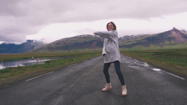 Glückliche-junge-Frau-tanzt-auf-Asphaltstraße-in-Island-und-etwas-Spaß,-Slow-motion