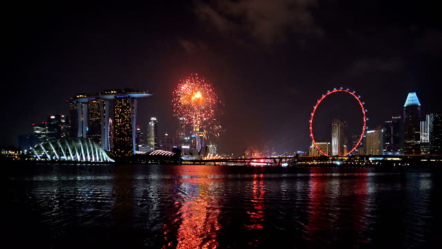 Fuegos-artificiales-del-día-nacional-de-Singapur-en-la-ciudad-de-centro-de-la-ciudad-de-Singapur-en-Marina-Bay-area-en-la-noche.-Edificios-financieros-de-distrito,-la-Noria-y-rascacielos.
