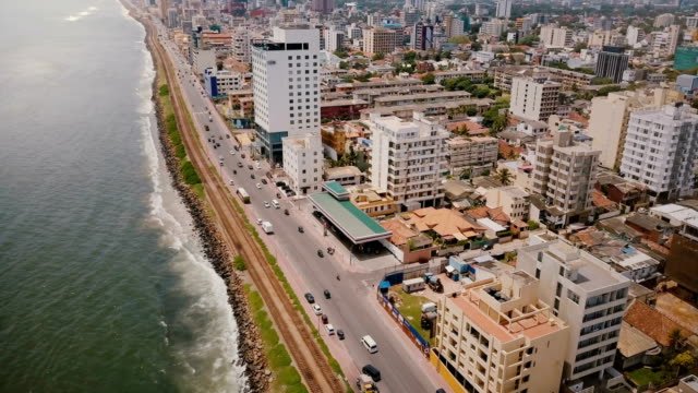 Drone-flying-above-Colombo-coast,-Sri-Lanka.-Amazing-aerial-view-of-city-street-traffic,-modern-buildings-and-ocean