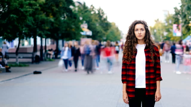 Time-lapse-portrait-of-confedent-young-woman-standing-alone-in-the-street-on-summer-day-and-looking-at-camera-while-people-are-whizzing-around-in-hurry.