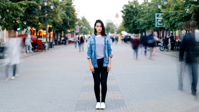 Time-Lapse-Porträt-der-gestresste-junge-Frau-allein-im-Zentrum-der-Stadt-trägt-Jeans-und-Jeansjacke-und-Blick-in-die-Kamera,-während-Menschen-vorbeifahren.