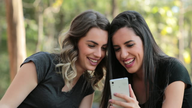 Echte-Freunde-zusammen-im-freien-Handy-überprüfen.-Mädchen-auf-der-Suche-und-halten-Smartphone-chatten-Klatsch-austauschen