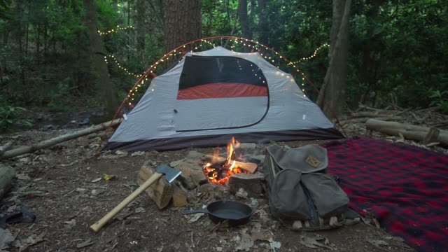 Bushcraft-camp-site-in-the-wilderness-with-campfire,-axe,-and-blanket.